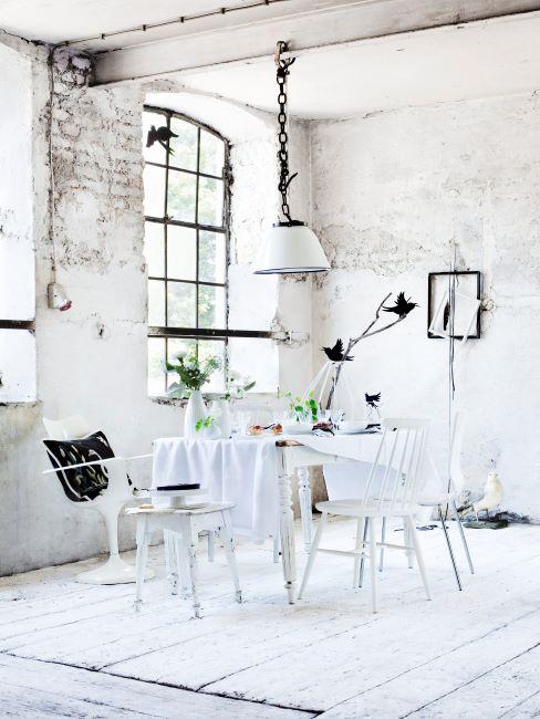 salle à manger dans une pièce aux murs de briques peints en blanc, suspension industrielle et mobilier blanc