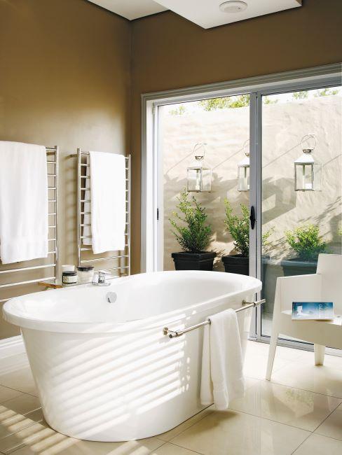 salle de bain avec baignoire, fauteuil design blanc et grande fenêtres ouvert sur le jardin