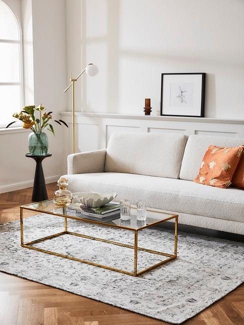 petit salon avec tapis vintage, table basse dorée et en verre, petit canapé beige et coussin terracotta