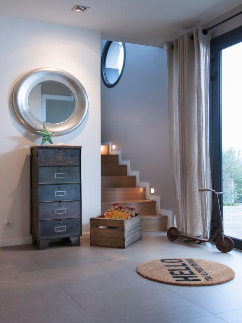 miroir mural rond avec grand cadre, petit tapis rond en jute, caisse en bois, commode haute en bois, murs blanc cassé
