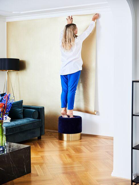une femme sur un pouf en train de poser papier peint sur le mur
