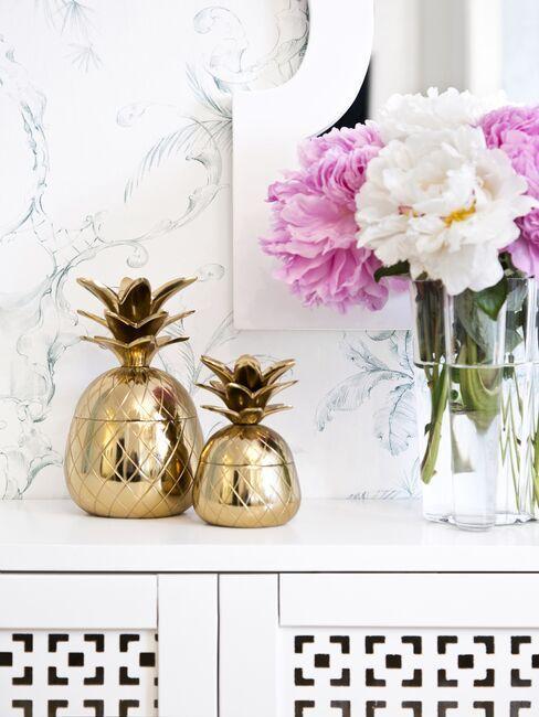 console avec bouquet des pivoines dans un vase transparent, boîtes décoratives ananas dorées