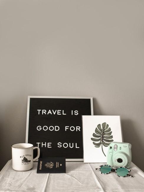 Tableau avec une inscription sur le voyage, une tasse et un appareil photo polaroid posés sur une table