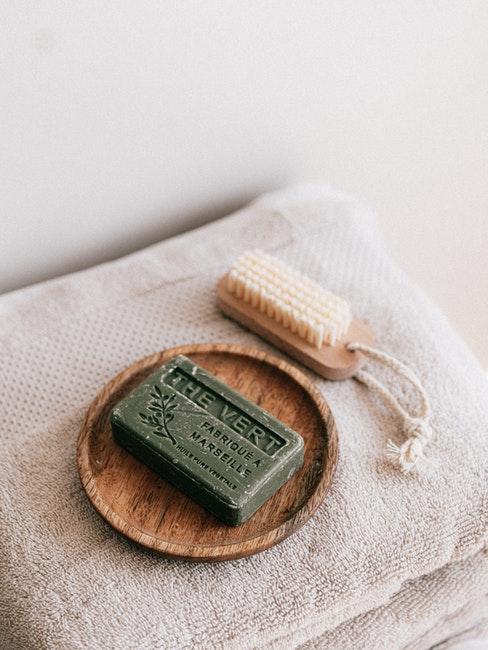 Savon vert sur assiette en bois, brosse de gommage et serviettes de bains crème