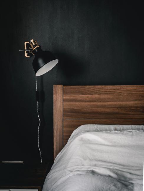 zoom sur lit en bois dans une chambre à coucher aux murs anthracite et lampe de chevet moderne