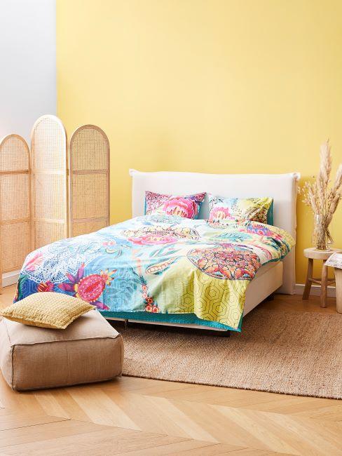 linge de lit multicolore, chambre à coucher murs jaunes, pouf, tapis, paravan en matière naturelle