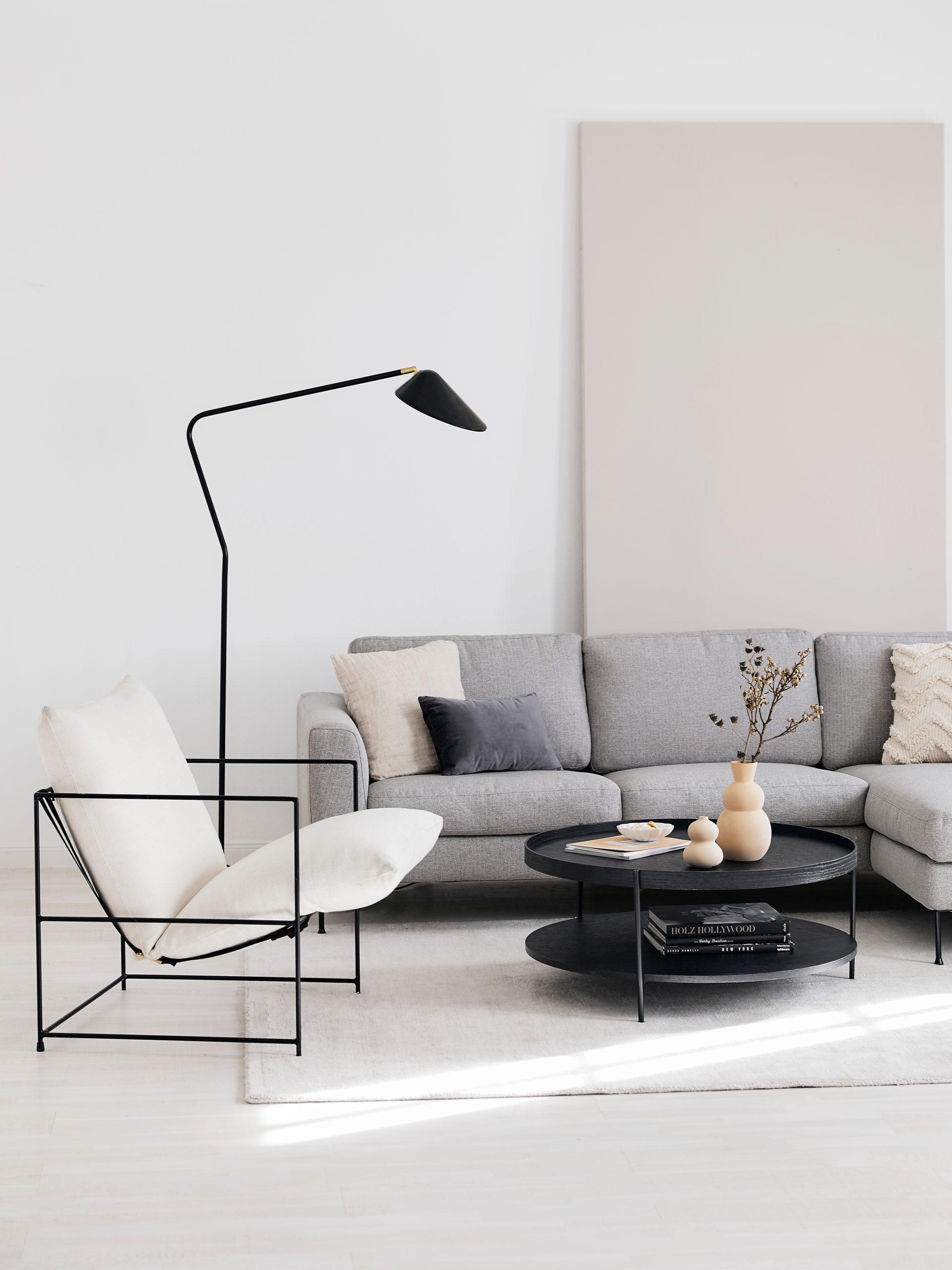 Salon avec canapé gris, fauteuil blanc, lampadaire noir et table basse ronde noire
