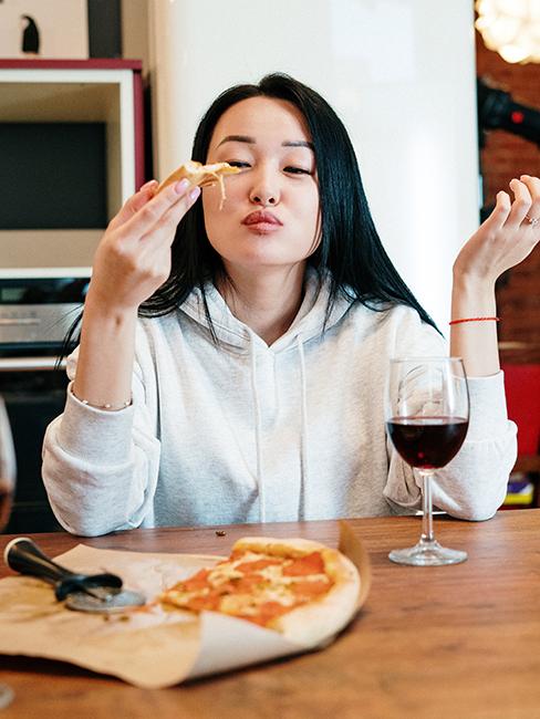 une jeune fille entrain de manger une part de pizza avec un verre de vin