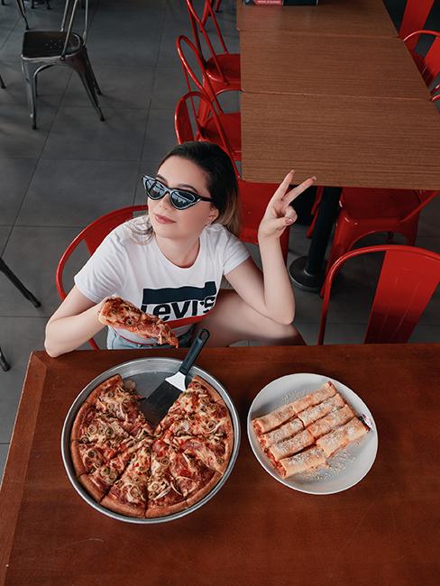 une jeune fille avec des lunettes de soleil entrain de manger de la pizza