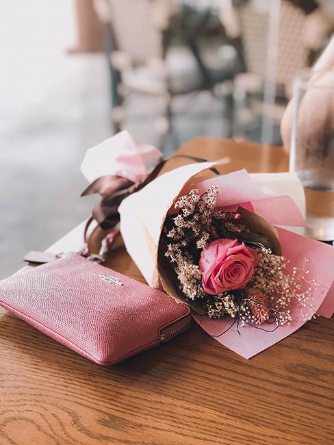 Un bouquet de roses avec un portemonnaie rose posés sur une table en bois
