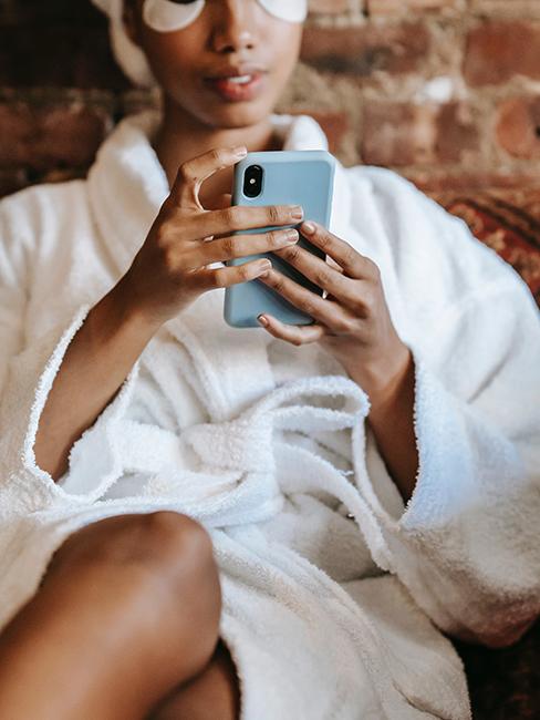 personne en peignoir blanc entrain de regarder son téléphone portable