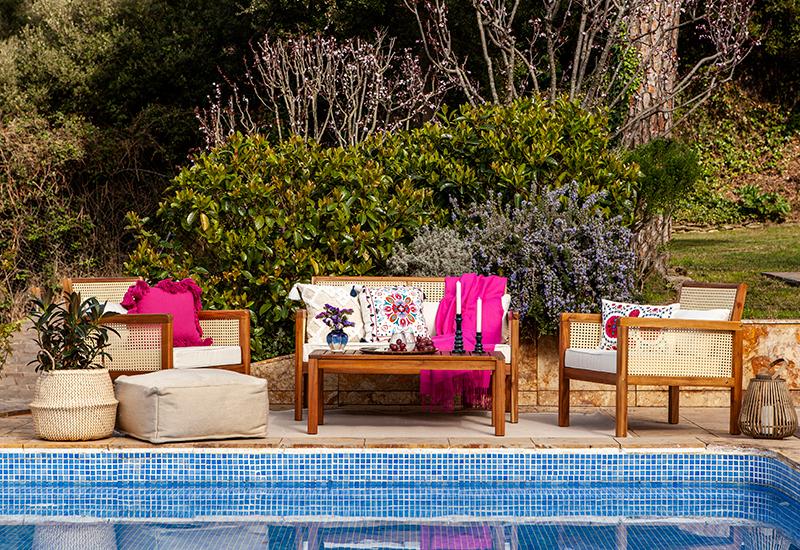 terrasse avec salon de jardin en bois et coussins roses au bord d'une piscine