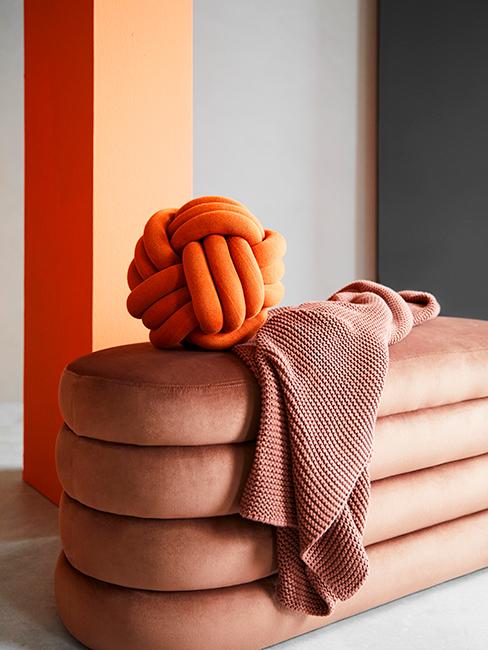 coussin orange en forme de tricol posé sur un banc en velours terracotta