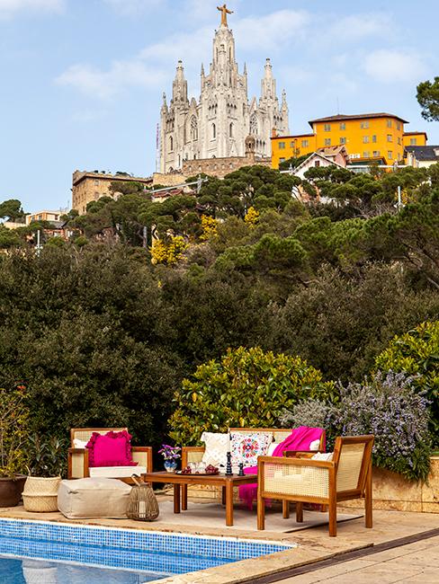 terrasse au bord d'une piscine avec salon de jardin en bois et coussins roses