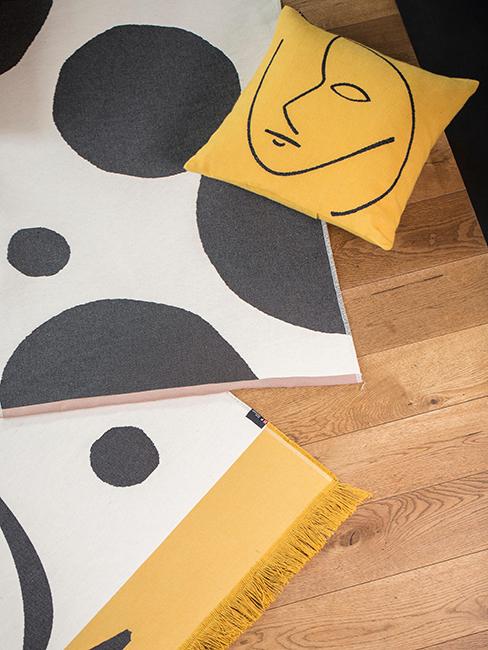 coussin jaune avec motif visage posé au sol sur des tapis