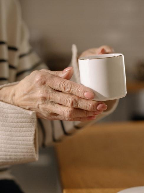 mains d'une personne agée avec une jolie tasse à café en porcelaine