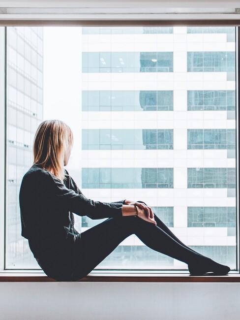 femme assise au rebord d'une grande fenêtre regardant en mode zen, niksen