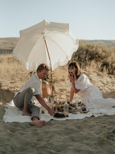 couple assis dans le sable, parasol blanc, plage, pique-nique en amoureux
