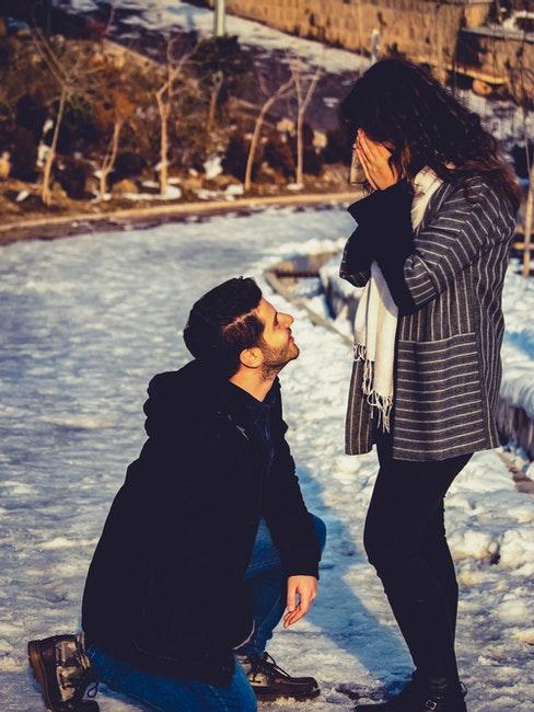 jeune homme en train de faire sa demande en mariage à genou dans la neige devant une femme