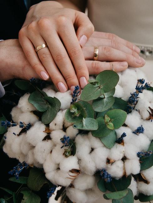 mains couple marié posées l'une sur l'autre, les alliances en évidence, bouquet en fleurs de coton