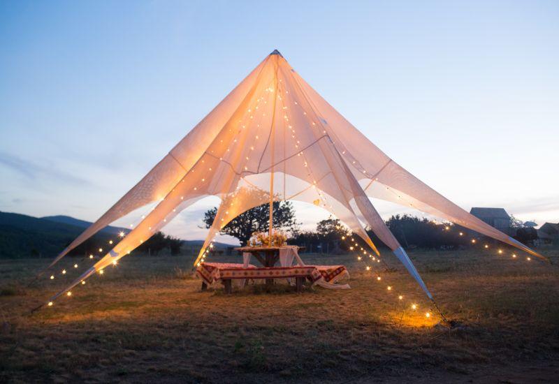 Mariage en extérieur sous une tente au coucher du soleil éclairage table en bois