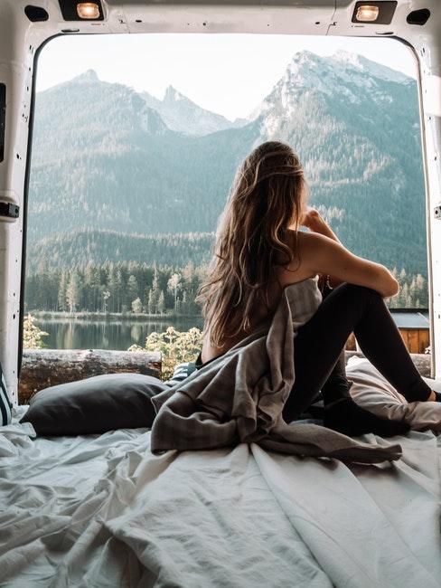 femme assise sur son matelas dans un van avec une vue sur les montagnes