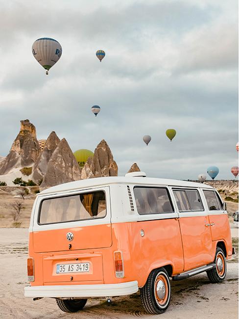 van vintage orange dans le desert avec des montgolfières