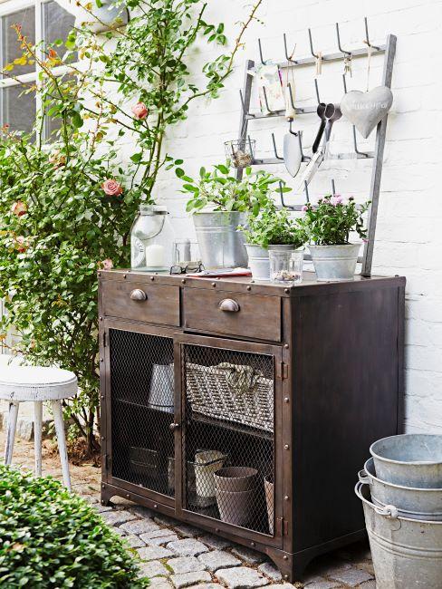 mur extérieur décoré des roses et d'une vieille commode à outils de jardinage et des pots de plantes vertes