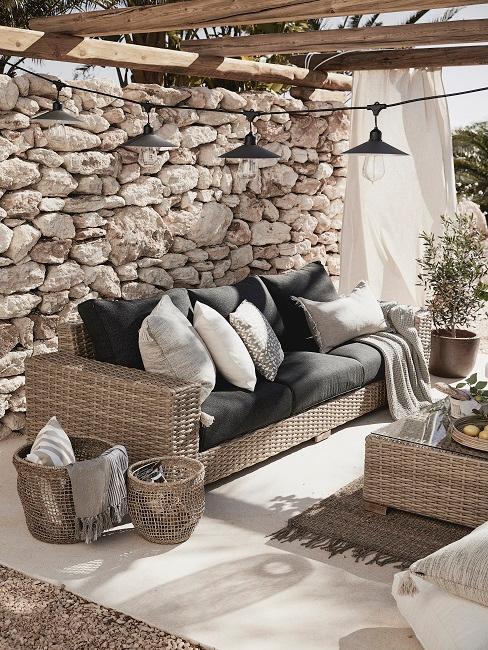 jardin style méditerranéen avec mur de pierre, poutres en bois et salon de jardin en osier