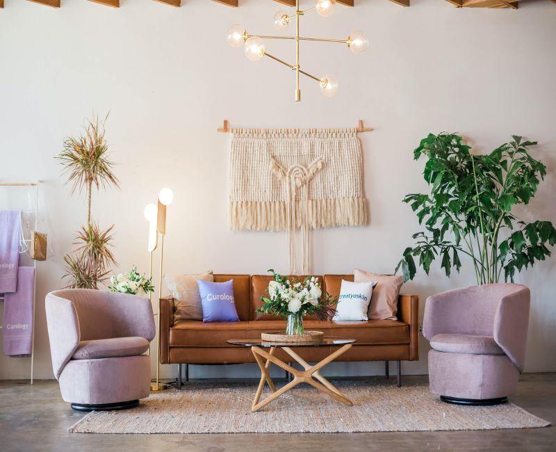 séjour avec grande suspension dorée, moderne, fauteuils lilas, canapé en cuir marron, grand macramé sur le mur, petite table en bambou, grandes plantes tropicales en pot