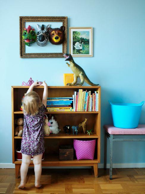 meuble avec jouet enfant, peluches et livres avec cadre avec masque de dragon, zèbre et ours et petite fille qui joue