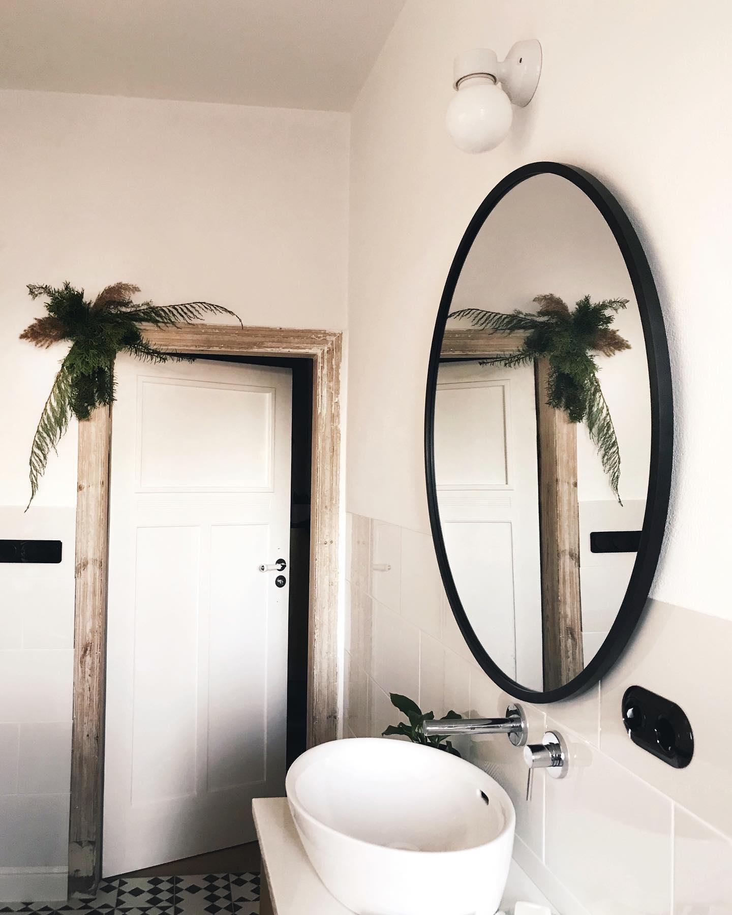 évier de toilettes blanc avec un miroir mural rond et un chassis de porte en bois