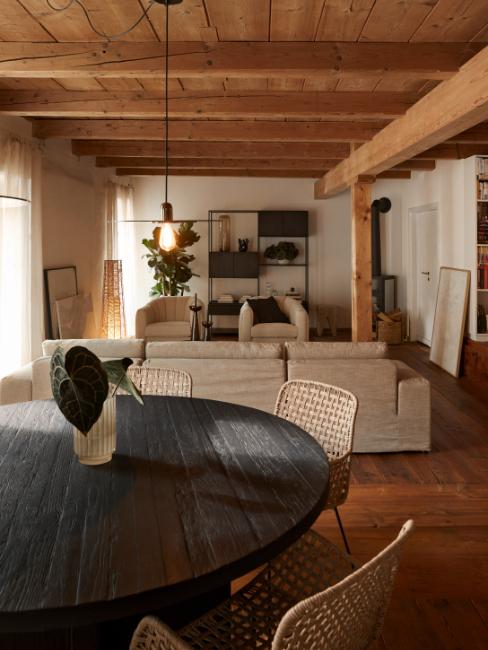 salon salle à manger avec plafond en bois, table ronde noire et canapé beige