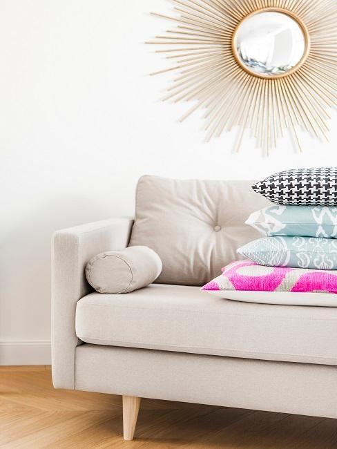 Divano chiaro di fronte a parete chiara con specchio a forma di sole dorato