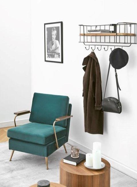 attaccapanni da muro con cappotto e cappello appesi accanto a poltrona verde