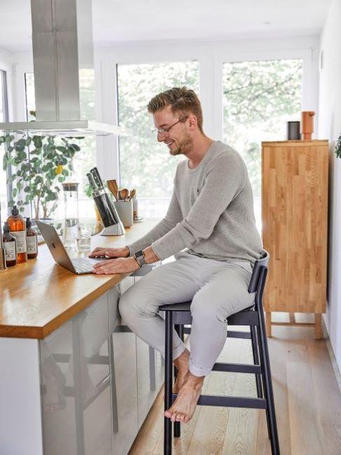 uomo che lavora al computer seduto al bancone della cucina