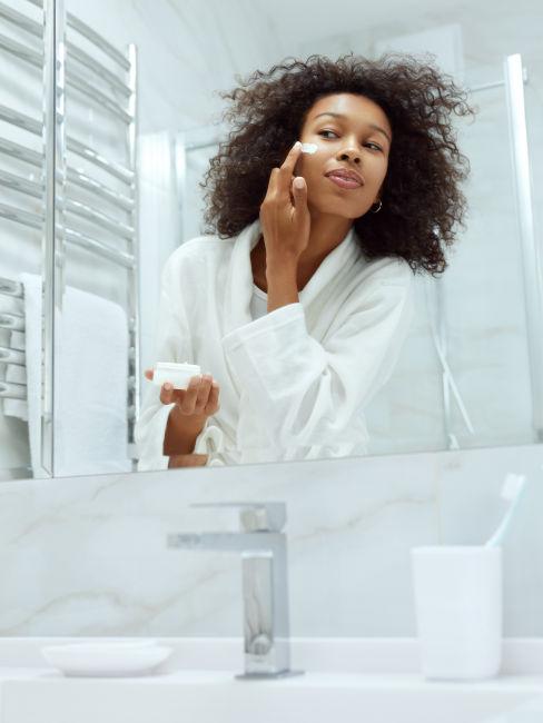 Donna allo specchio che applica crema idratante sul viso