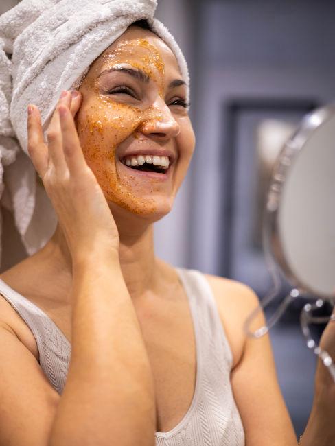 Donna che ride e massaggia uno scrub sul viso