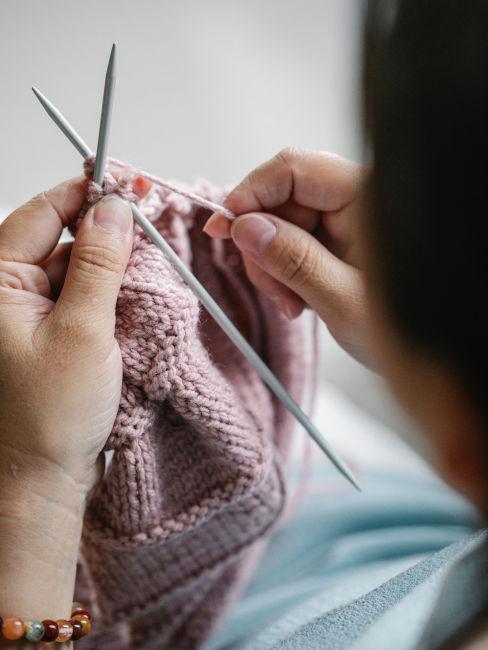 mani di ragazza che lavora a maglia con cotone rosa