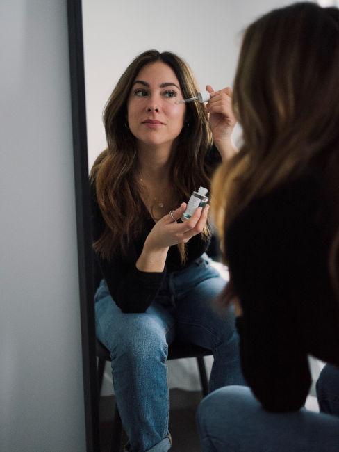 ragazza allo specchio che applica un siero sul viso