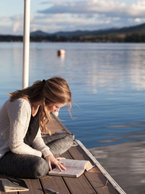 ragazza che legge un libro in riva al lago