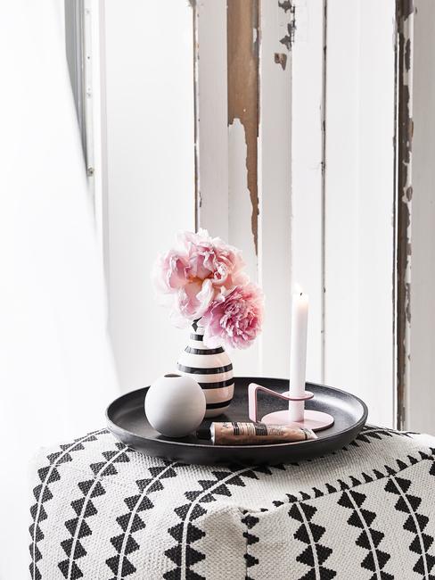 Witte poef met patroon met zwart decoratief dienblad met vaas uit keramiek met bloemen en kaars