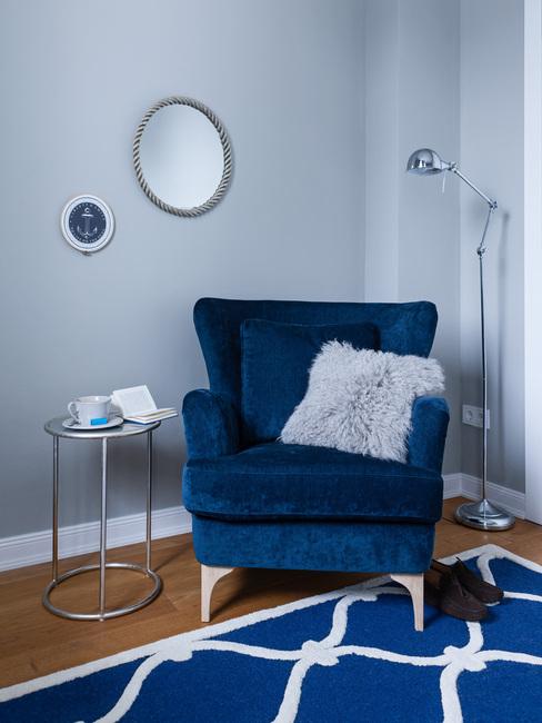 Donkerblauwe fluwelen fauteuil met sierkussen op blauw vloerkleed