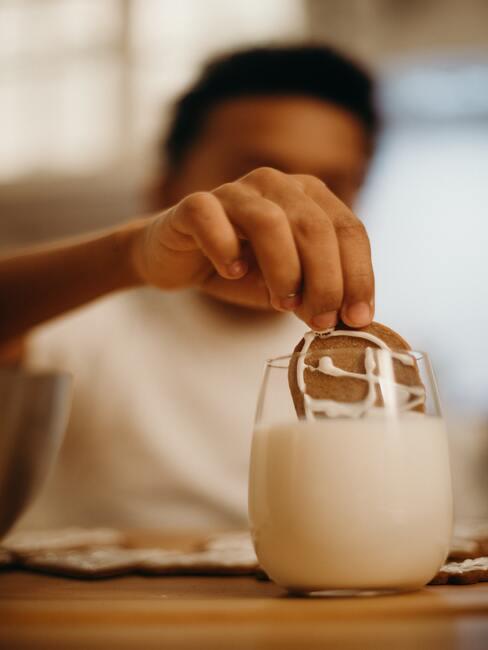 Een kind dat een koekje in een glas melk doet