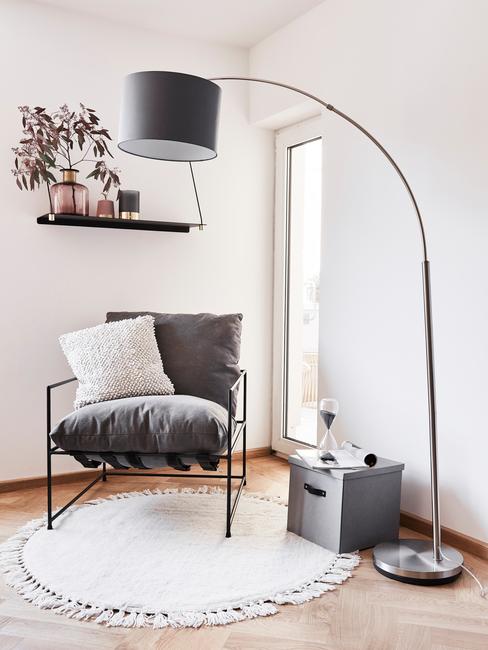 Zwarte metalen fauteuil met sierkussen in beige naast een vloerlamo