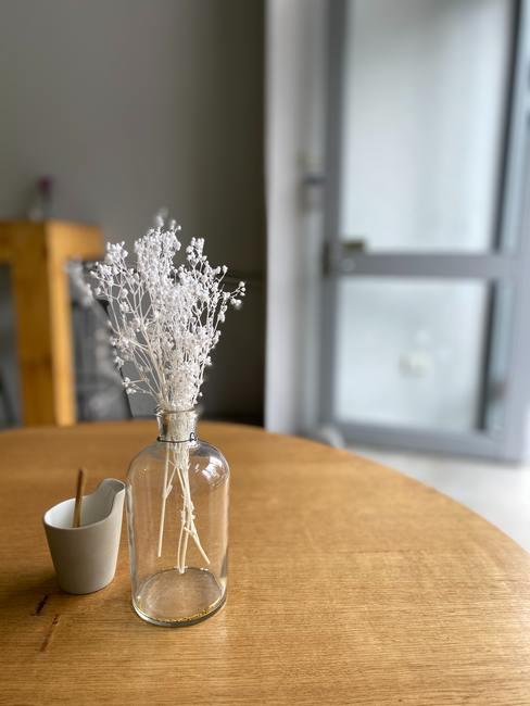 Kunsttakje in een transparante glazen vaas op een houten ronde tafel