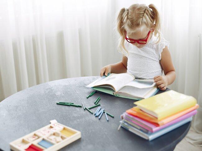 Meisje leest en kleurt aan tafel met raam op de achtergrond
