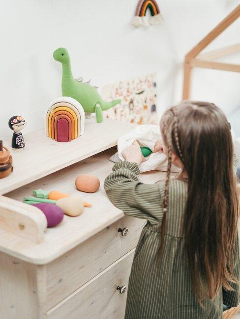 Meisje speelt met groenten speelgoed op houten bureau met speelgoed op de achtergrond