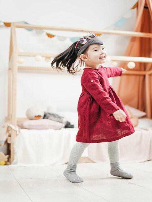 Meisje in rode jurk speelt in meisjes slaapkamer met bed op de achtergrond