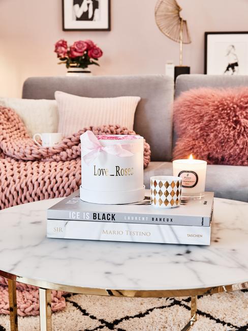 Een grijze bank met sierkussens en zachte chunky knit plaid naast een marmeren salontafel met koffietafelboek en geurkaars